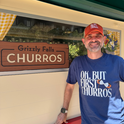 man wearing an orange trucker hat that reads "ok, but first churros"
